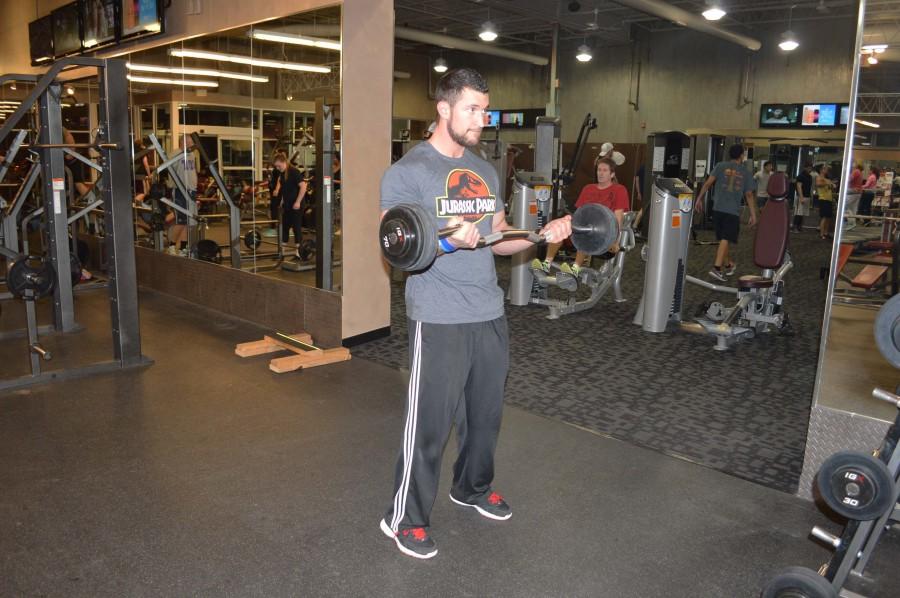 Campbell does bicep curls with the curl bar by standing shoulders width apart, holding the bar with both hands, and raising his hands without moving his shoulders. 

