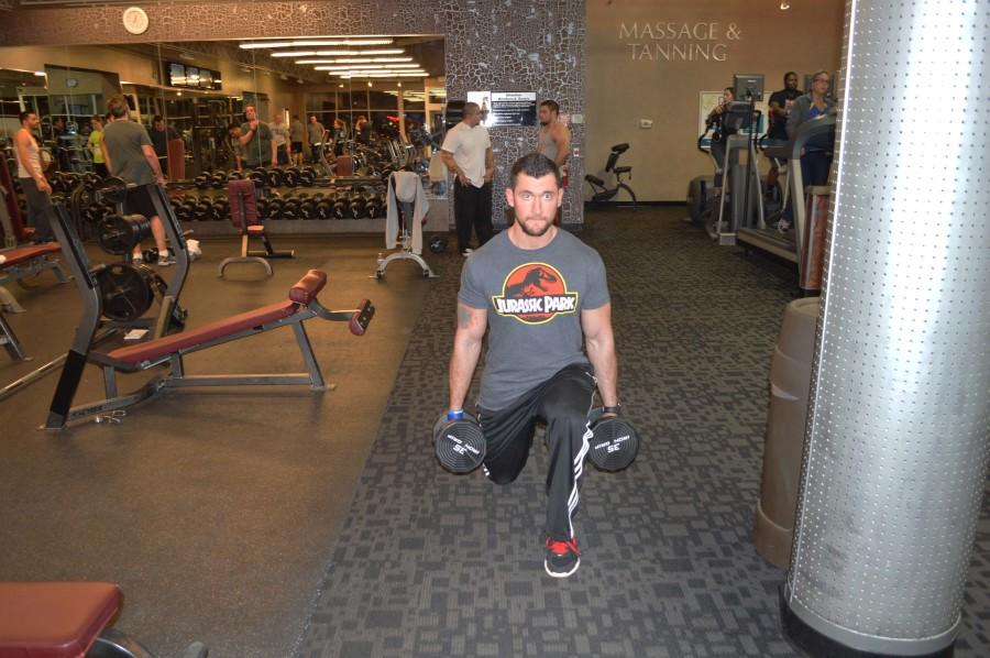 Campbell does some standing lunges while holding a dumbbell in each hand. He steps one foot forward and begins to bend his front knee until his knee makes a 90 degree angle. 
