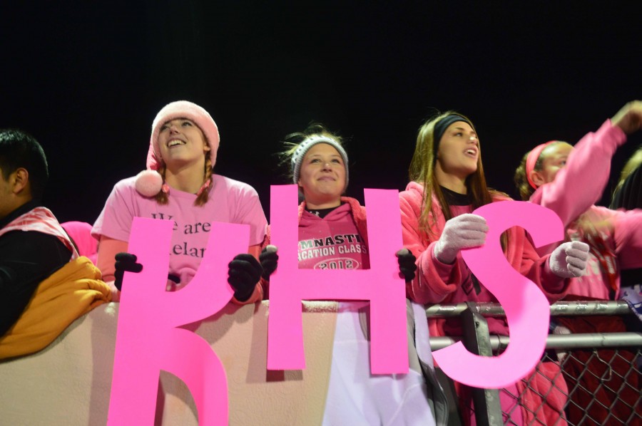 Seniors on the fence hold up bright pink letters for breast cancer awareness. 