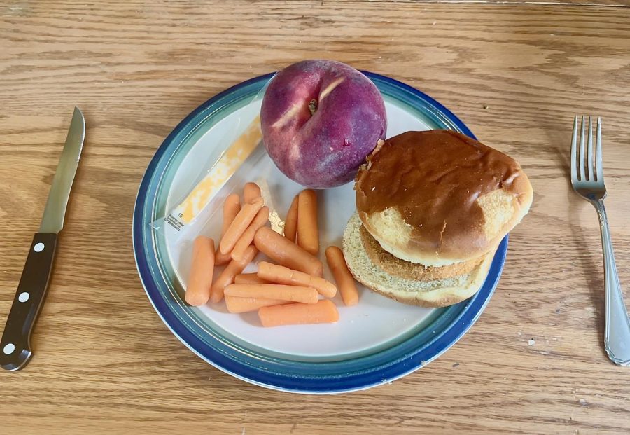 A plate sits on a kitchen table with a generally balanced meal: a chicken sandwich, baby carrots, a cheese stick and a peach. A healthy meal can look different for everyone but broadly, a meal should consist of fruits, vegetables, grains, protein and dairy.