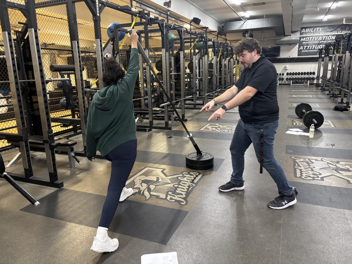 Kaneland High School football and track & field coach Trevor McKeown coaches an athlete in the West Gym weight room during track practice. Bonds with coaches can exist outside of games and practices and can become lasting connections.