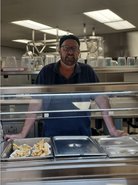 A cafeteria staff member works behind the counter serving fries.