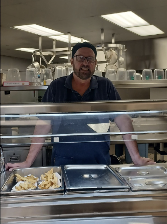 A cafeteria staff member works behind the counter serving fries.